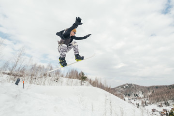 Naklejka na ściany i meble Snowboarder jumping from kicker in winter cloudy day
