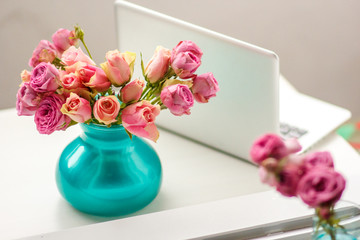 roses in a green vase on a table near a laptop