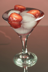 Cold cocktail with ice and strawberries seeds. Mirror background