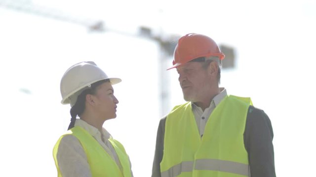 Two builders, a man and a young woman, are discussing work issues. Against the background of a crane.