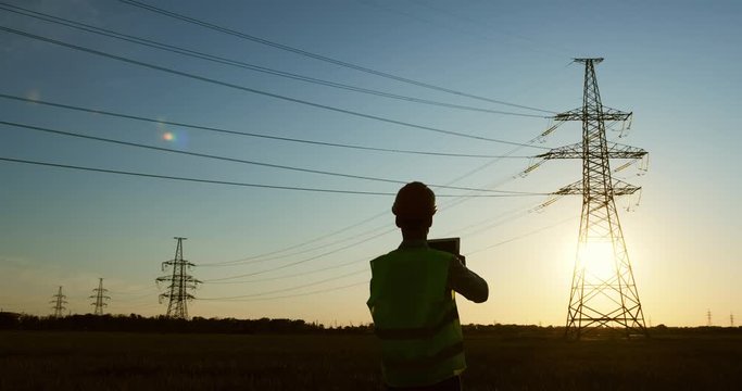 The power engineer conducts a power line state inspection using a tablet, sunset background.