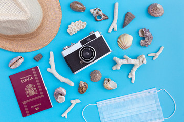 Top view of straw hat, protective face mask, passport, analog photo camera and beach shells on blue background. Coronavirus covid-19, summer vacation and travel concept.