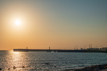 Fototapeta na wymiar Clear sky and bright sunset at sea port with a breakwater and a lighthouse