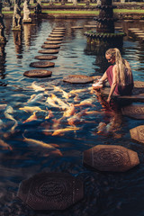 Woman feeding beautiful coloured fish in pond. Taman Tirtagangga temple on Bali