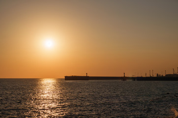 Fototapeta na wymiar Beautiful yellow and orange sunset over the sea. The sun goes down over the sea. Silhouette of sea port at sunset