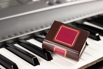 Close-up on the piano keys is a small decorative book. Playing by notes. Concept of romance and music