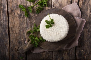 Suluguni cheese is cut into large pieces on a wooden round board. Garnished with parsley leaves,  and pepper.