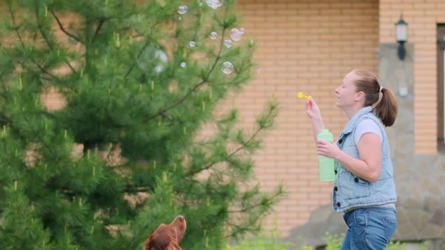playful dog is played outdoors with woman jumping for soap bubbles.