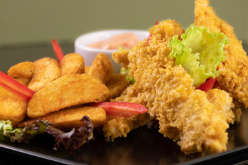 Close-up of delicious crispy fried chicken breast strips with wedges on black plate