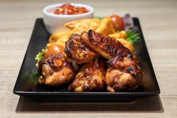 Great beer snack - spicy baked buffalo wings. BBQ wings with garnish of salad and wedges on black plate. Close up. Pub food.