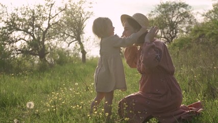 Beautiful young pregnant mother in an embroidered dress playing straw hat with her daughter, Little girl 2 years old in a dress.