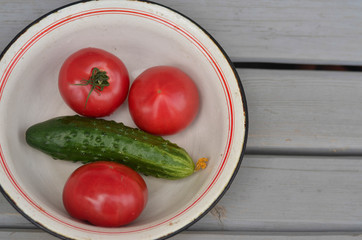 dry tomatoes with leaves and one cucumber in a plate on a wooden table