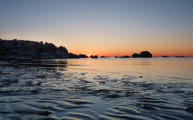 Southern coast of Finnish Gulf. Sand dunes with wave pattern. Baltic Sea water reflecting orange morning sky. Smooth transparent water, dark rocks. Blue hour turning to golden period. Estonia, Baltic