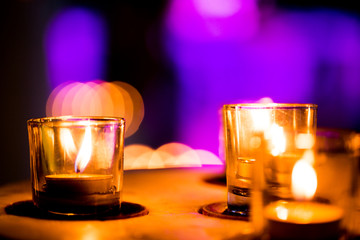 Flame of many candles burning on purple blurred background.