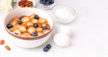 A wholesome tiny pancake cereal breakfast next to ingredients on a white plate. Copy space