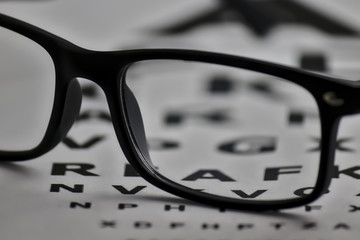 gafas colocadas sobre un folio con letras para poder graduar la vista - obrazy, fototapety, plakaty