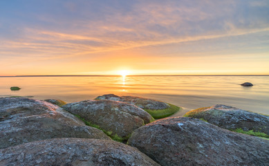 Southern coast of the Finnish Gulf. Rocks covered with green seaweed in the Baltic sea. Smooth transparent reflective water. Orange sunset markings under the low altitude clouds. Estonia, Baltic