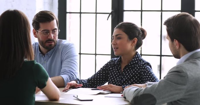 Head shot young indian businesswoman discussing working issues with motivated diverse partners at boardroom. Happy millennial colleagues developing project expansion strategy at brainstorming meeting.