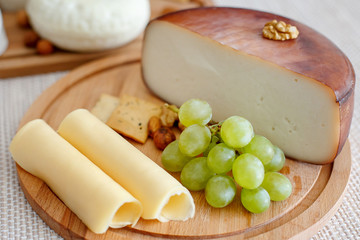 Cheese mix on a wooden plate decorated with grapes, nuts, salad and olives with cheese knifes 