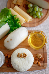 Cheese mix on a wooden plate decorated with grapes, nuts, salad and olives with cheese knifes 