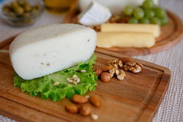 Cheese mix on a wooden plate decorated with grapes, nuts, salad and olives with cheese knifes 
