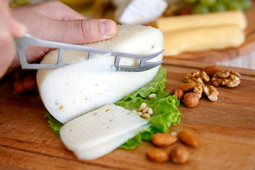 Chef slices the cheese. Cheese mix on a wooden plate decorated with grapes, nuts, salad and olives with cheese knifes 