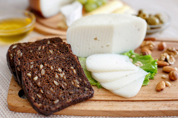 Cheese mix on a wooden plate decorated with grapes, nuts, salad, bread and olives with cheese knifes 