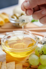Chef's hand dip the cheese in honey. Cheese mix on a wooden plate decorated with grapes, nuts, salad and olives with cheese knifes 