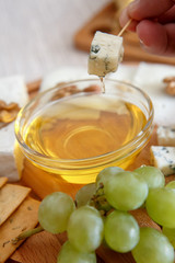 Chef's hand dip the cheese in honey. Cheese mix on a wooden plate decorated with grapes, nuts, salad and olives with cheese knifes 