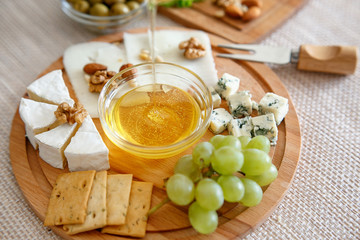 Chef pours honey. Cheese mix on a wooden plate decorated with grapes, nuts, salad and olives with cheese knifes 
