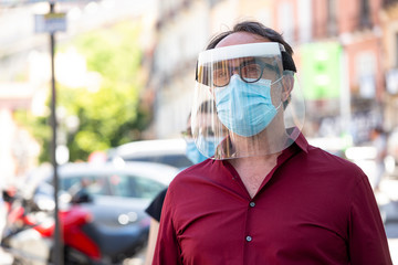 Uomo con mascherina facciale e visiera facciale in plexiglass in centro città