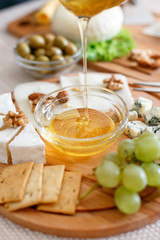 Chef pours honey. Cheese mix on a wooden plate decorated with grapes, nuts, salad and olives with cheese knifes 
