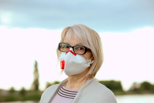 Portrait of aMature woman in 
protective respirator preventing an epidemic. A woman over 60 years old with gray hair in a gray blouse looking at the camera thoughtfully in the nature where the river. 