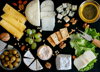 Cheese mix on a black desk, decorated with grapes, nuts, salad and olives with cheese knifes 