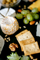 Cheese mix on a black desk, decorated with grapes, nuts, salad and olives with cheese knifes 