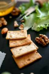 Cheese mix on a black desk, decorated with grapes, nuts, salad and olives with cheese knifes 