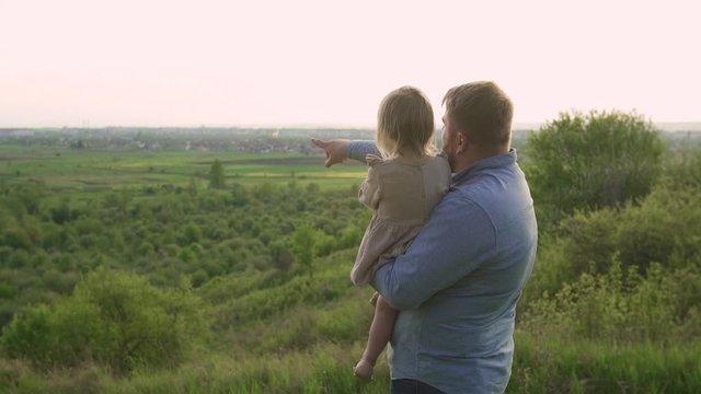 father with child, standing on the mountain. holds a child in his arms and shows her the city