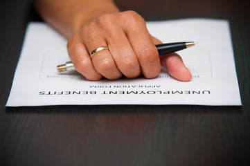 Hand with pen on unemployment benefits form.