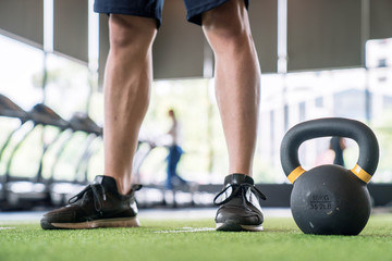 The young man in the gym stood in front of the dumbbell, He exercises by lifting weights.