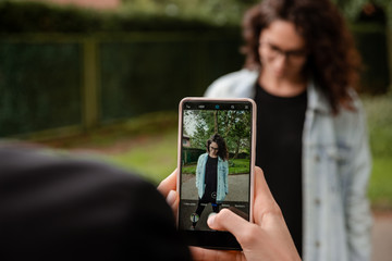 Young woman taking a picture of her friend with a mobile phone in the park.