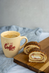 Two slices of sponge roll on wooden cutting board and a cup of coffee on the table at kitchen