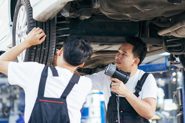 automotive mechanic man checking under car condition in garage at auto repair shop on lifter hoist....