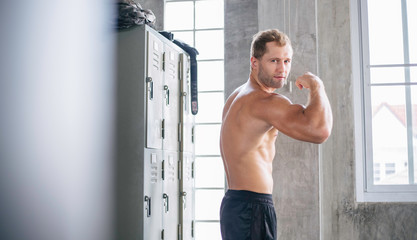 Obraz premium Portrait of Caucasian man showing his biceps muscle at gym fitness locker. muscular strong men workout exercise for better health. people back to normal lifestyle concept with copy space
