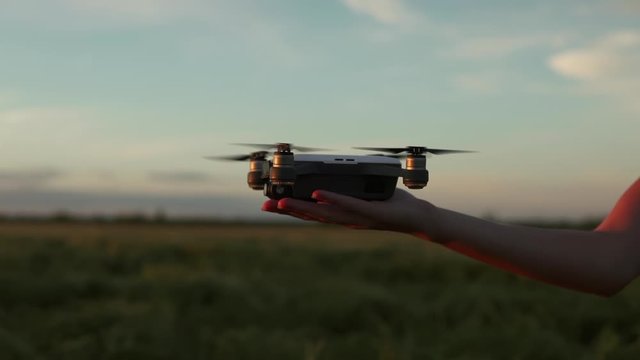 Woman's hand controls drone fly to the sky in summertime sunset in the field. Faceless girl set copter from hands. Wireless technology, gadget, internet concept. Professional equipment for filming