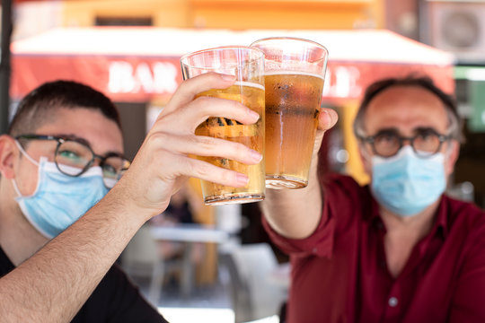 padre e figlio con mascherina brindano al tavolo con un boccale di birra felici per la ritrovata libert&agrave;