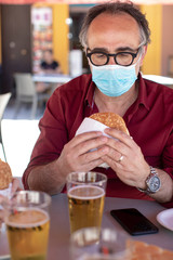 Uomo con mascherina chirurgica è seduto  al bar in attesa di mangiarsi un panino con la cotoletta e l birra 