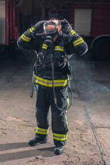 Fototapeta premium Portrait of a fireman wearing firefighter turnouts and helmet. Dark background with smoke and blue light.