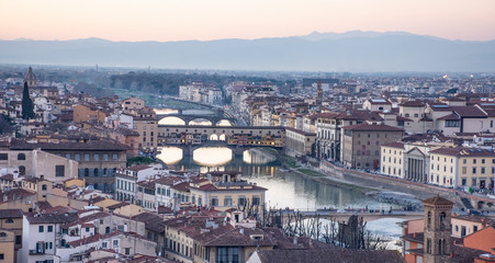 Fototapeta na wymiar Vista de ciudad de Florencia atravesada por río en el atardecer con colinas de fondo