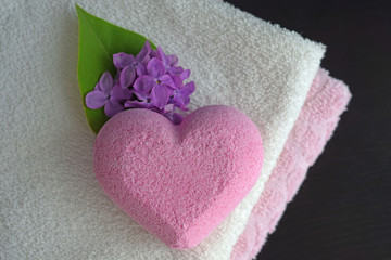 Bath salt in the shape of a heart with a light fragrance of lilac.Soft towels and a flower on a black background.