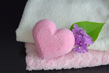 Bath salt in the shape of a heart with a light fragrance of lilac.Soft towels and a flower on a black background.